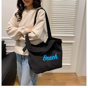 Detailed shot of a black canvas tote bag with blue Beach print worn by a model