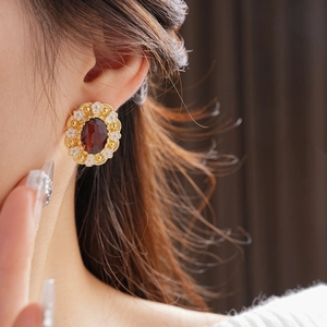 Close-up of vintage gold flower earrings with oval red gemstone on a female model
