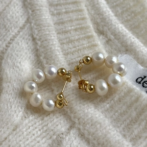Elegant pearl hoop earrings with gold beads displayed on a soft white knit sweater