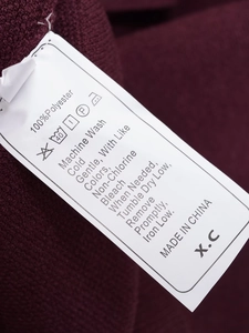 Detailed fabric texture and white care label showing 100% polyester on a maroon knit top