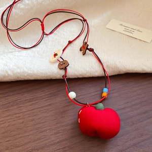 Macro detail of red fabric apple pendant with rustic wooden beads on a woven cord necklace