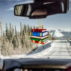 Flat acrylic Christmas stack of books ornament hanging from car mirror on snowy road