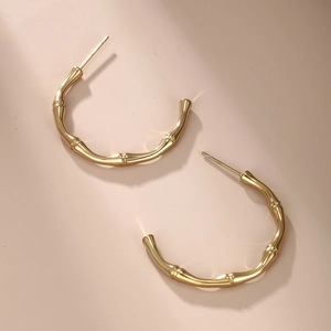 Elegant gold bamboo-textured C-shape hoop earrings for women on a soft pink background