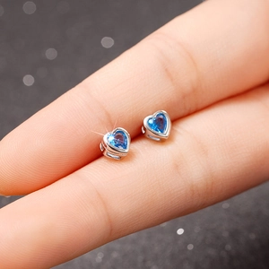Macro view of dainty blue heart-shaped stud earrings held between fingers for scale