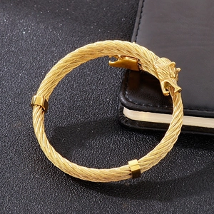 Close-up of golden dual wolf head steel wire bracelet on black textured surface