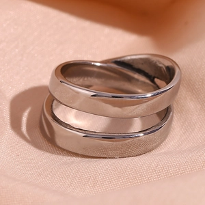 Macro shot of polished silver-tone double layer crossover rings on soft pink fabric