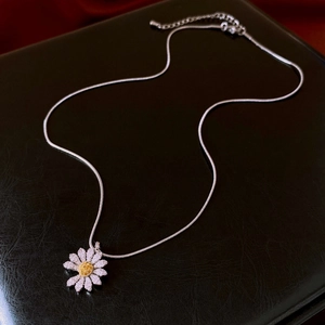 Detailed close-up of zircon daisy pendant on silver snake chain over black leather