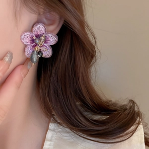 Gros plan de boucles d'oreilles fleurs en tissu violet avec perles sur un modèle femme