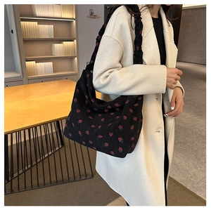 Detail of strawberry print corduroy tote bag with ruffled strap worn by a model