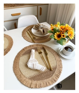 Detail of round woven placemats with beige gradient patterns and fringed edges on table