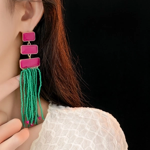 Close-up of long tassel earrings with green seed beads and magenta enamel rectangles