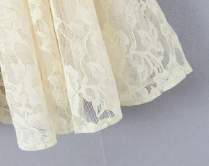 Close-up of beige lace fabric texture and floral patterns on the flared skirt hem