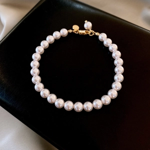 Detail view of white pearl bracelet featuring a gold clasp and a small round charm on silk