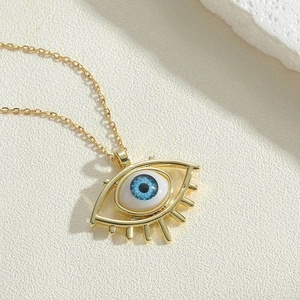 Detailed shot of a gold Evil Eye pendant necklace with blue pupil and textured stone background