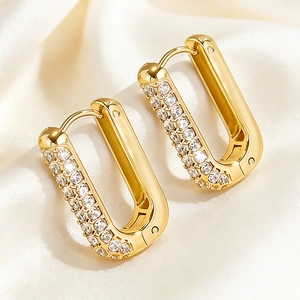 Macro shot of gold U-shaped hoop earrings with sparkling cubic zirconia on beige silk