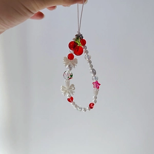 Detail of beaded phone strap with red cherry charm and white pearl accents held by hand