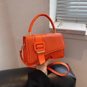 Detalle de un bolso bandolera naranja de cuero sintético con textura de cocodrilo y hebilla cuadrada