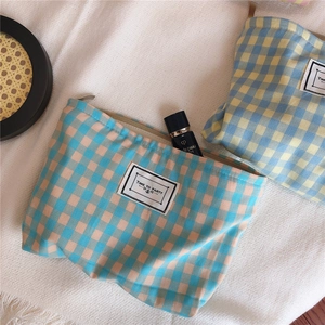 Close-up of checkered cotton makeup bags with zippers on a soft textured cream blanket