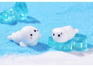 Close-up of two miniature resin seals on a blue textured ice surface for DIY decor