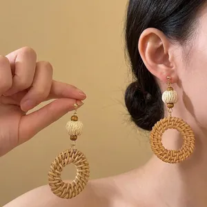 Detail view of handmade woven rattan drop earrings with wooden beads on model