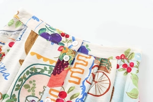 Detail view of woven skirt featuring white buttons and colorful fruit pattern print