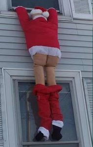 Outdoor festive decoration showing a funny Santa Claus climbing a wall with bare buttocks
