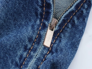 Makrodetail aus blauem Denim mit Metallreißverschluss und orangen Kontrastnähten