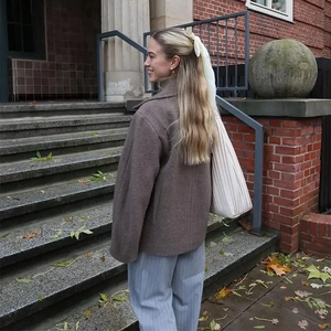 Close-up of brown tweed double-breasted jacket paired with a white pleated tote bag