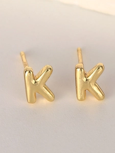 Macro detail of polished gold-plated letter K stud earring with a glossy metallic finish