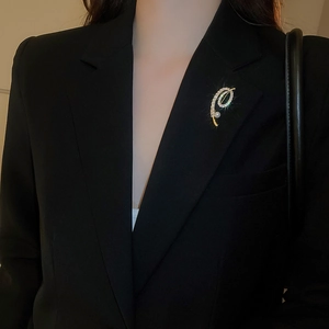 Détail d'une élégante broche dorée avec zircons et perle sur un blazer noir chic