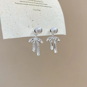 Macro detail of silver bow earrings with lace texture and elegant hanging pearls