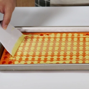 Spreading batter into a fish-shaped orange silicone mold with a white scraper tool
