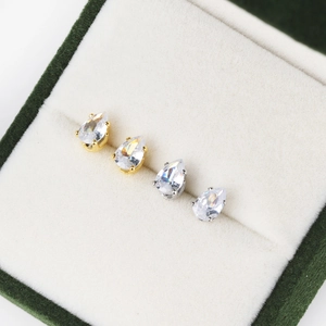 Macro shot of gold and silver teardrop zircon earrings in a premium dark green velvet jewelry box