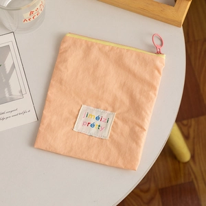 Apricot fabric cosmetic pouch with yellow zipper and jiméizi pretty logo on white table
