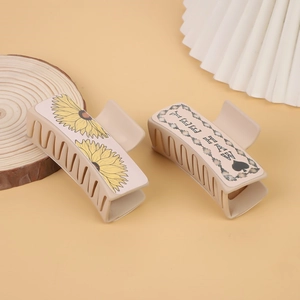 Detail of beige hair clips with sunflower design and DREAM lettering on a wooden base