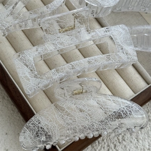 Detail of transparent lace pattern hair claws with gold springs on a beige tray