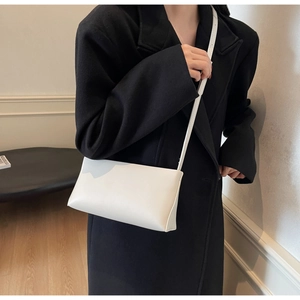 Minimalist white leather crossbody bag shown on a model wearing a black winter coat