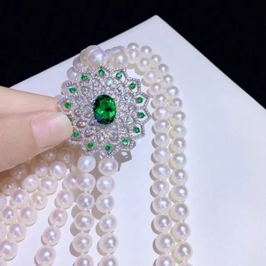 Elegant multi-strand pearl necklace featuring a floral gold pendant with emerald stones