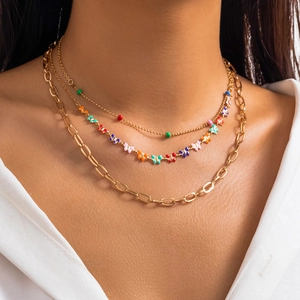 Close-up of triple-layered gold necklaces with colorful butterfly pendant and chain links