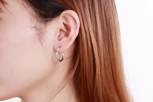 Close-up of 20mm silver stainless steel hoop earrings worn on ear showing polished finish