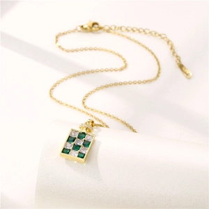 Collier flacon de parfum à damier doré avec cristaux verts sur socle blanc