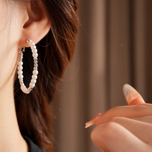 Detailed view of large hoop earrings with alternating silver beads and white pearls on a model