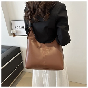 Brown leather tote bag worn over the shoulder showing high-capacity design and texture