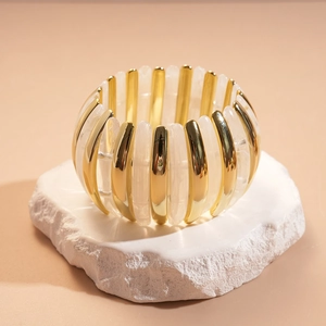 Detailed view of an elastic beaded bracelet with gold metal and cream acrylic bars
