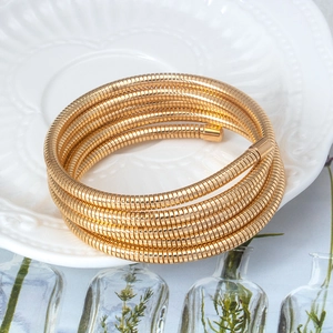 Detail of a golden multi-layer coil spring bracelet on a white embossed decorative plate