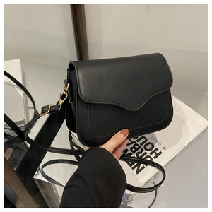 Detail of black crossbody bag featuring a unique wavy flap and elegant gold hardware