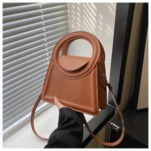 Detail view of a brown structured handbag with unique ring handle and matte leather texture