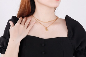 Detail of a layered golden musical guitar pendant necklace worn on a black outfit