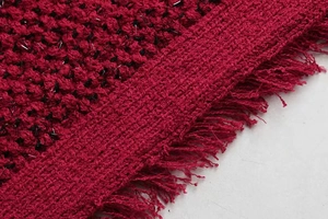 Gros plan sur un tissu en tweed rouge avec fils argentés et détails de franges