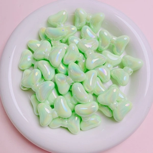 Detailed view of pale green iridescent bow-shaped beads for DIY jewelry making